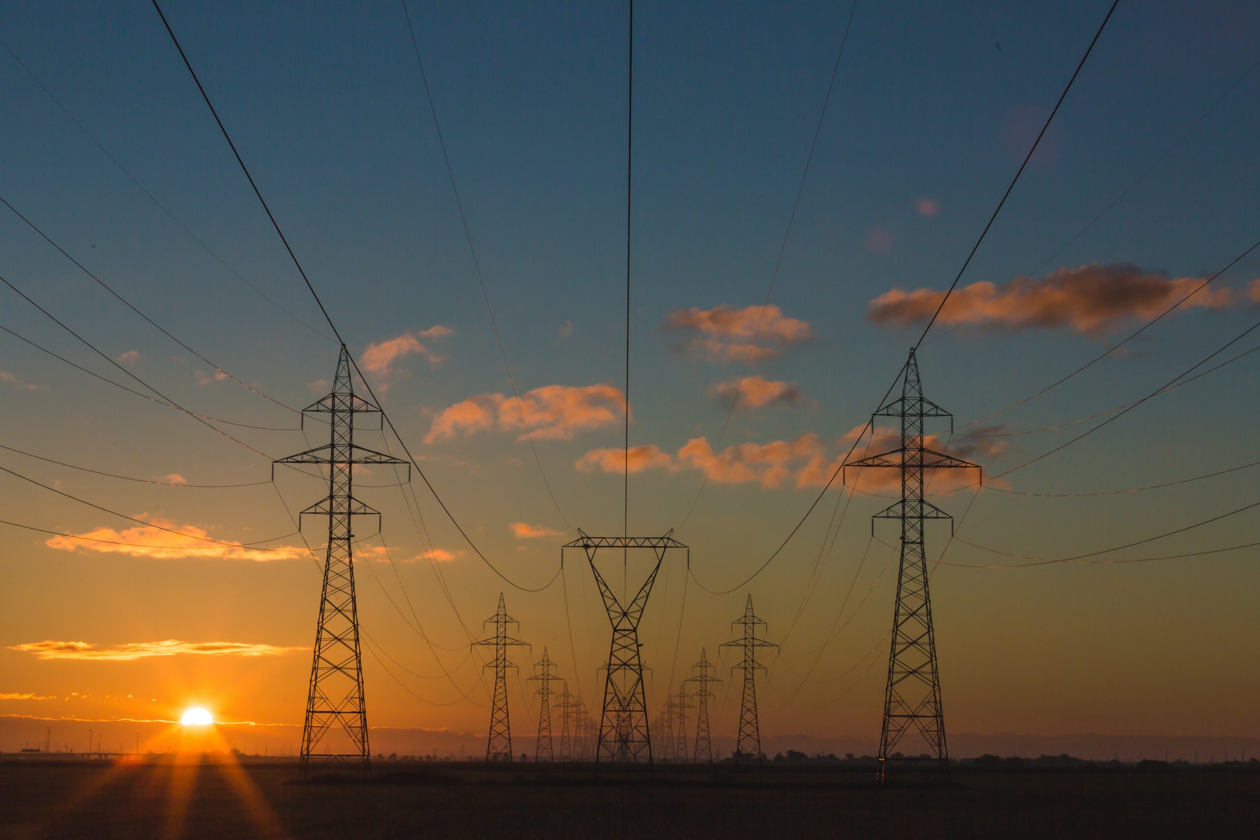 A landscape photograph of electricity pylons with a sunset behind and a few clouds in the sky.