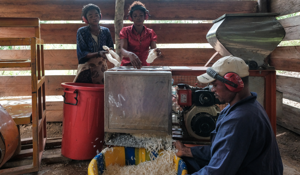 A photo of three people inside a barn, standing around a machine that is shredding food for animals.