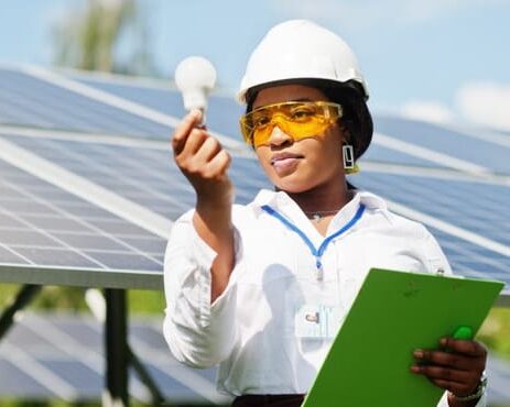 female engineer holding up a lightbulb with a solar panel behind her