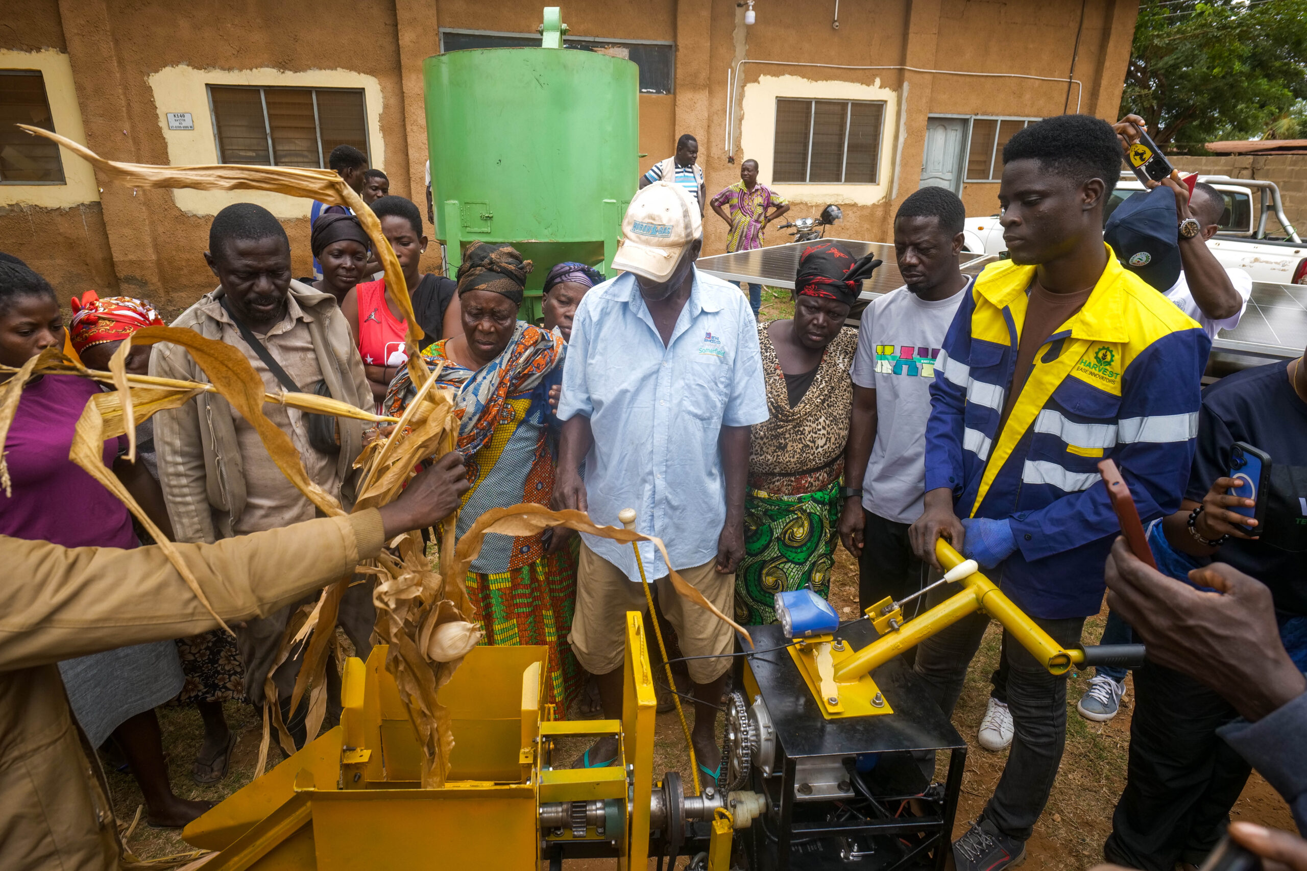 A group of people stand around looking at a new innovation that is being piloted. One person holds a dried leaf and places it into a machine for processing.