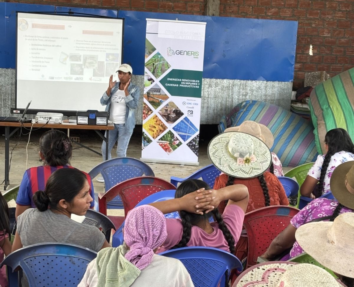 A photo taken at a conference. There are many women sat in chairs facing forward, with one woman speaking to the group. There is a GENERIS banner behind her and a projector.